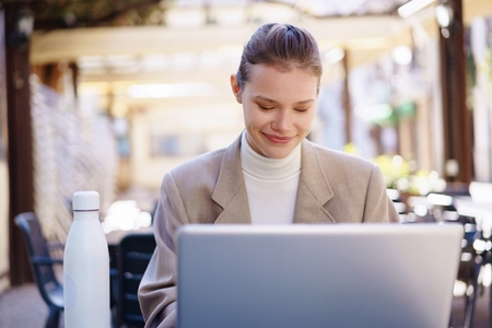 A young professional works on her laptop outdoors at a cafe  enjoying fresh air and sun