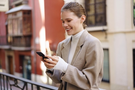 A Happy and Smiling Woman Engaged Deeply with Her Smartphone in a Lively Urban Setting A Happy and Smiling Woman Engaged Deeply with Her Smartphone in a Lively Urban Setting