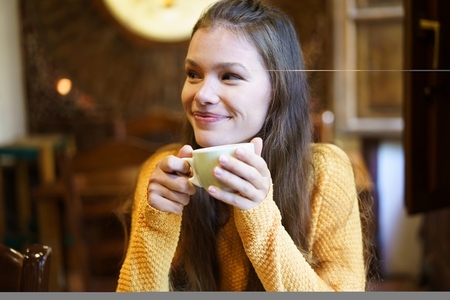 Cheerful and Happy Young Woman Enjoying a Warm Beverage While Relaxing in a Cozy Cafe setting Cheerful and Happy Young Woman Enjoying a Warm Beverage While Relaxing in a Cozy Cafe setting