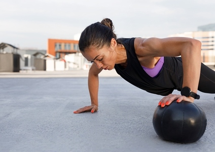 Young muscular female athlete doing push ups and using medicine ball  Woman in sportswear using medicine ball for strength exercises