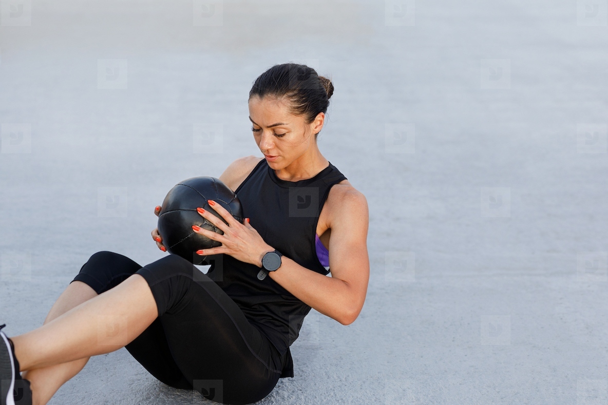 Woman in black fitness wear holding a medicine ball and practicing outdoors