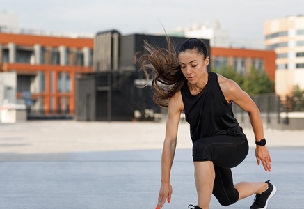 Young woman athlete with fit muscular body doing warming up exercises on the roof during a day