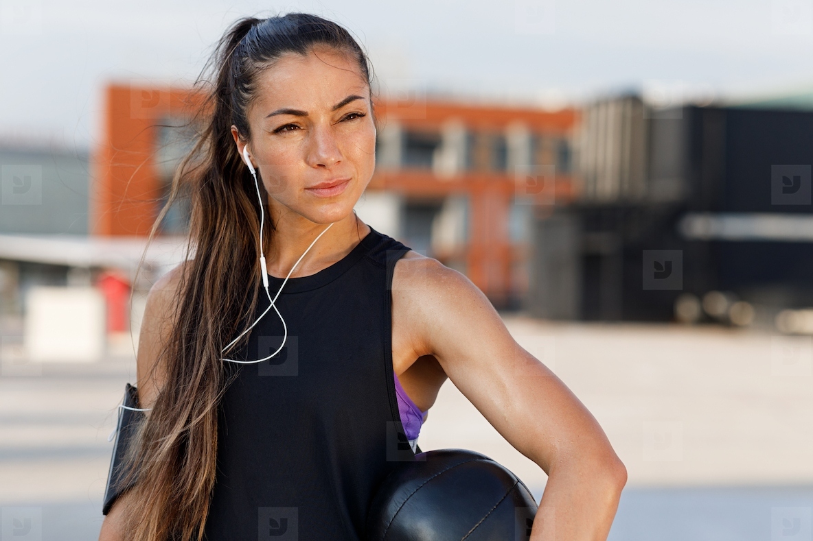 Confident female athlete with medicine ball wearing headphones Portrait of a young woman relaxing with medicine ball during workout