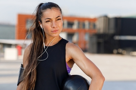 Confident female athlete with medicine ball wearing headphones  Portrait of a young woman relaxing with medicine ball during workout