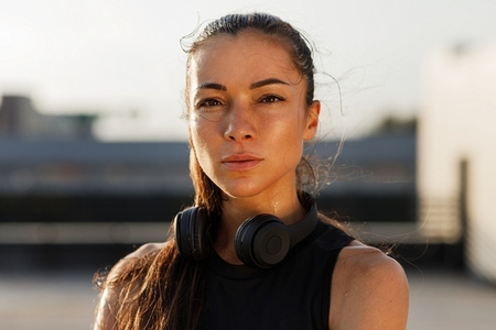 Close up high detailed portrait of a young sportswoman with smooth skin  wearing wireless headphones and standing outdoors
