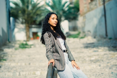 A Chic Young Woman Confidently Posing in a Lively Urban Setting Surrounded by Palms A Chic Young Woman Confidently Posing in a Lively Urban Setting Surrounded by Palms