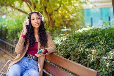 A Young Woman is Joyfully Enjoying Music While Outdoors in a Beautiful Park Setting A Young Woman is Joyfully Enjoying Music While Outdoors in a Beautiful Park Setting