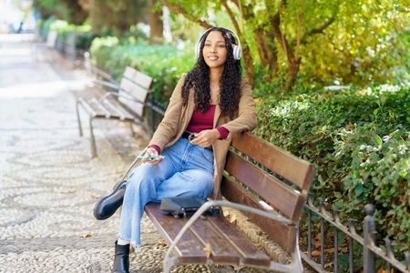A Young Woman Happily Enjoys Listening to Music While Sitting in a Beautiful Park Setting