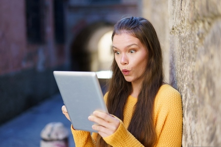 A Surprised Young Woman Engaged with Her Tablet While in an Urban Setting Filled with Life