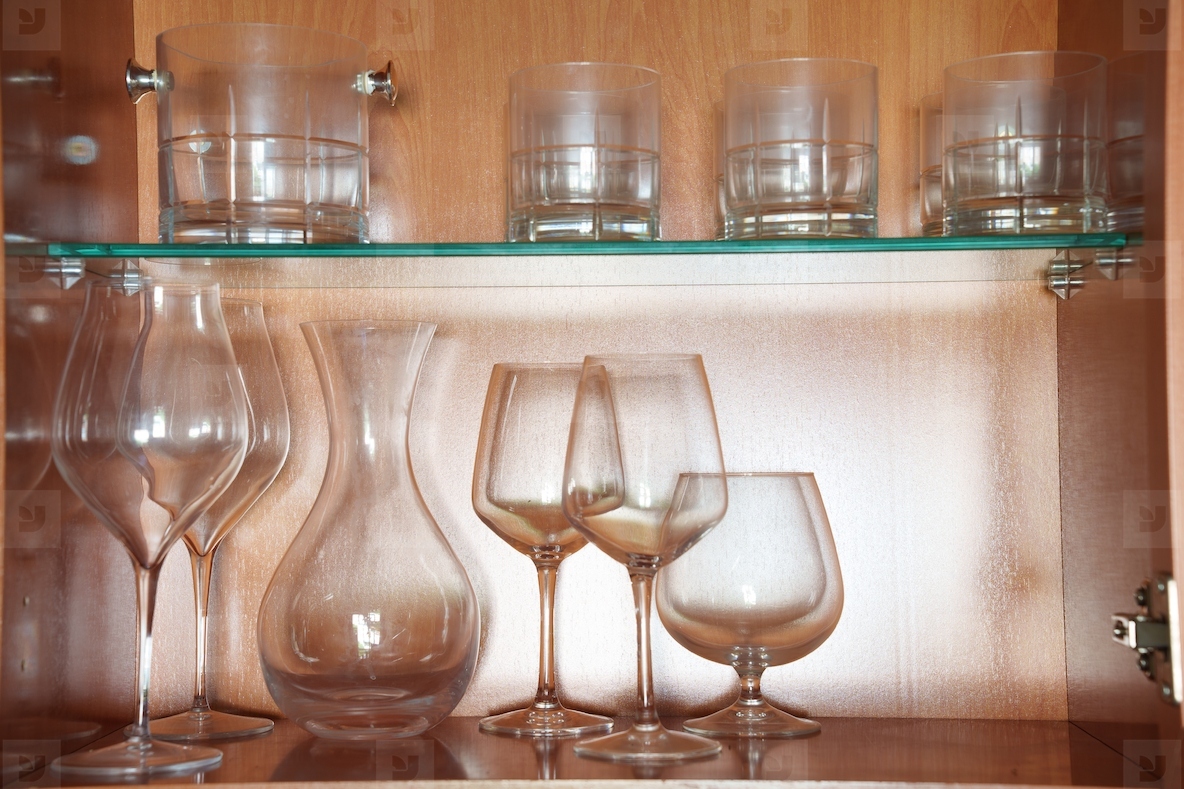 Luxurious glass collection showcased with soft amber illumination Sophisticated assortment of crystal glasses accentuated by warm backlighting against textured