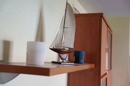 Cozy nautical scene  Serene maritime display on rustic wooden shelf with ceramics  Charming miniature sailboat scene showcasing vintage coastal charm in cozy interior