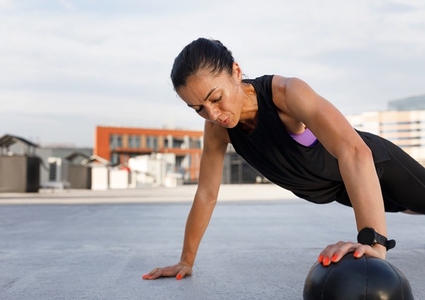 Young muscular female practicing push ups with a medicine ball outdoors  Woman doing an intense workout outdoors with medicine ball