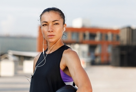 Portrait of a young confident female in headphones  standing on the roof and holding medicine ball