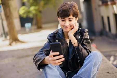 A joyful teenager is engaged with their smartphone while enjoying the outdoors today