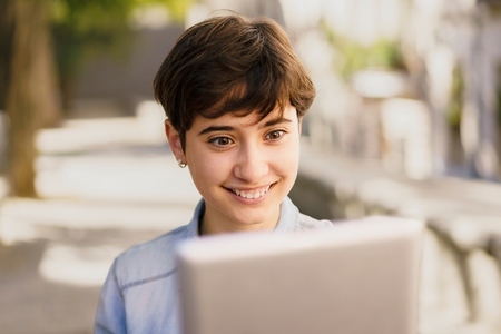 A Happy Young Girl Enjoying a Video Call with Her Laptop While Sitting Outdoors in Sunshine A Happy Young Girl Enjoying a Video Call with Her Laptop While Sitting Outdoors in Sunshine