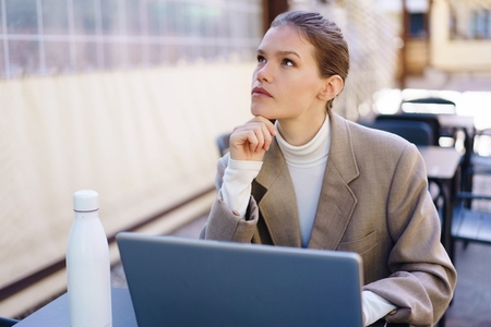 A Thoughtful Young Woman Engaged in Working on Her Laptop While Enjoying a Cozy Cafe Setting