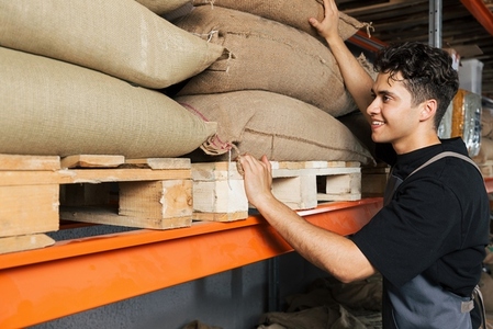 Barista at warehouse choosing a bag with beans  Young male at the shelfs in warehouse  with bags full of beans