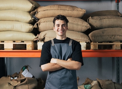 Portrait of young confident male worker in apron at warehouse  Male with crossed arms wearing apron standing at warehouse