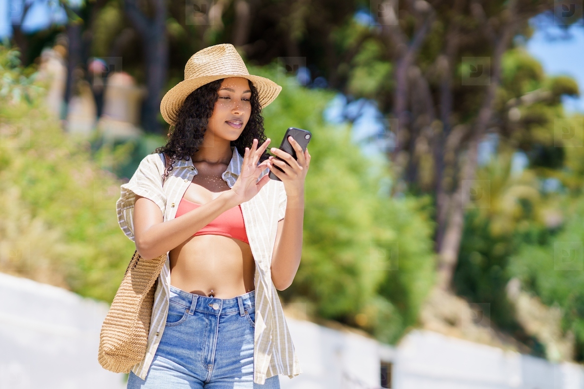 A Stylish Young Woman Holding a Smartphone Dressed in a Trendy Summer Outfit Outdoors