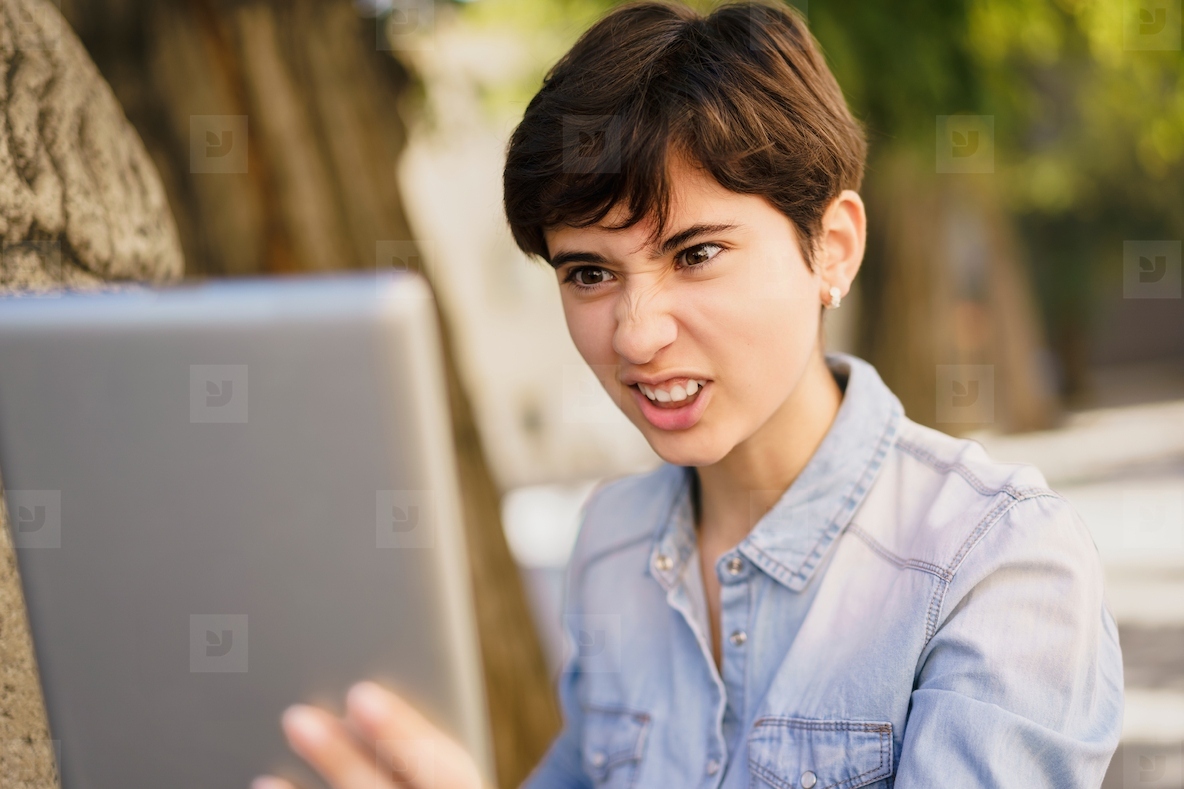 A frustrated young woman exhibiting her reaction to a laptop screen while outdoors in nature