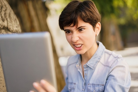 A frustrated young woman exhibiting her reaction to a laptop screen while outdoors in nature
