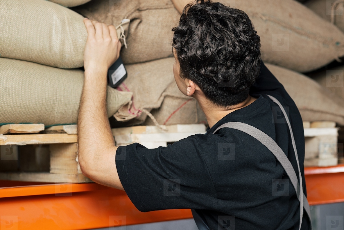 Back view of a young warehouse worker looking for the right coffee bag on the shelf