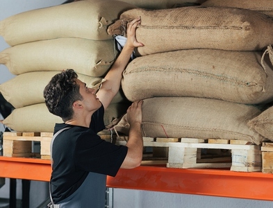 Warehouse worker moving a bag on a shelf Young employee in an apron working at a warehouse adjusting bags of coffee beans on the shelf Warehouse worker moving a bag on a shelf Young employee in an apron working at a warehouse adjusting bags of coffee beans on the shelf