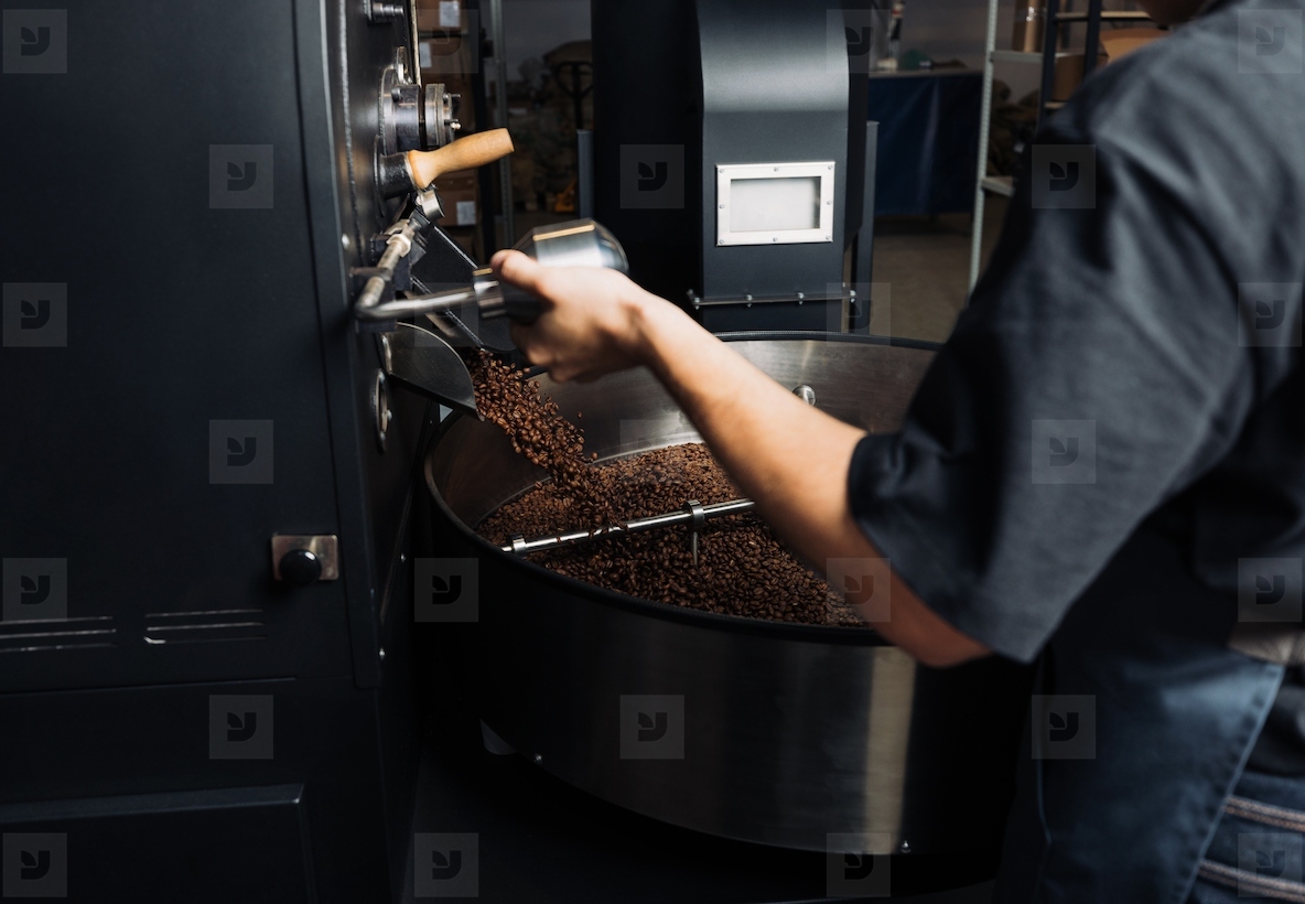 Unrecognizable worker opens a door at a coffee machine with fresh roasted beans Employee at the roasting coffee production machine