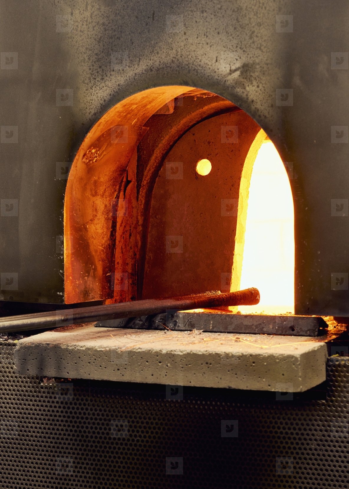 Tools in arched opening of hot glassblowing furnace