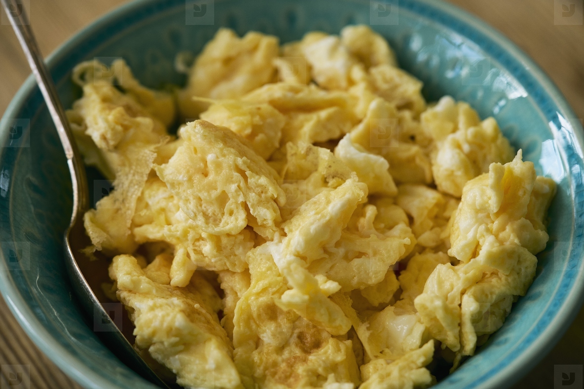 Close up of scrambled eggs in bowl with spoon