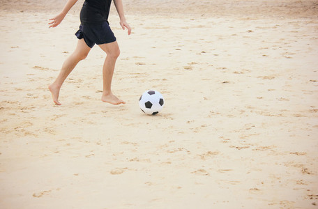 Man playing soccer ball on beach