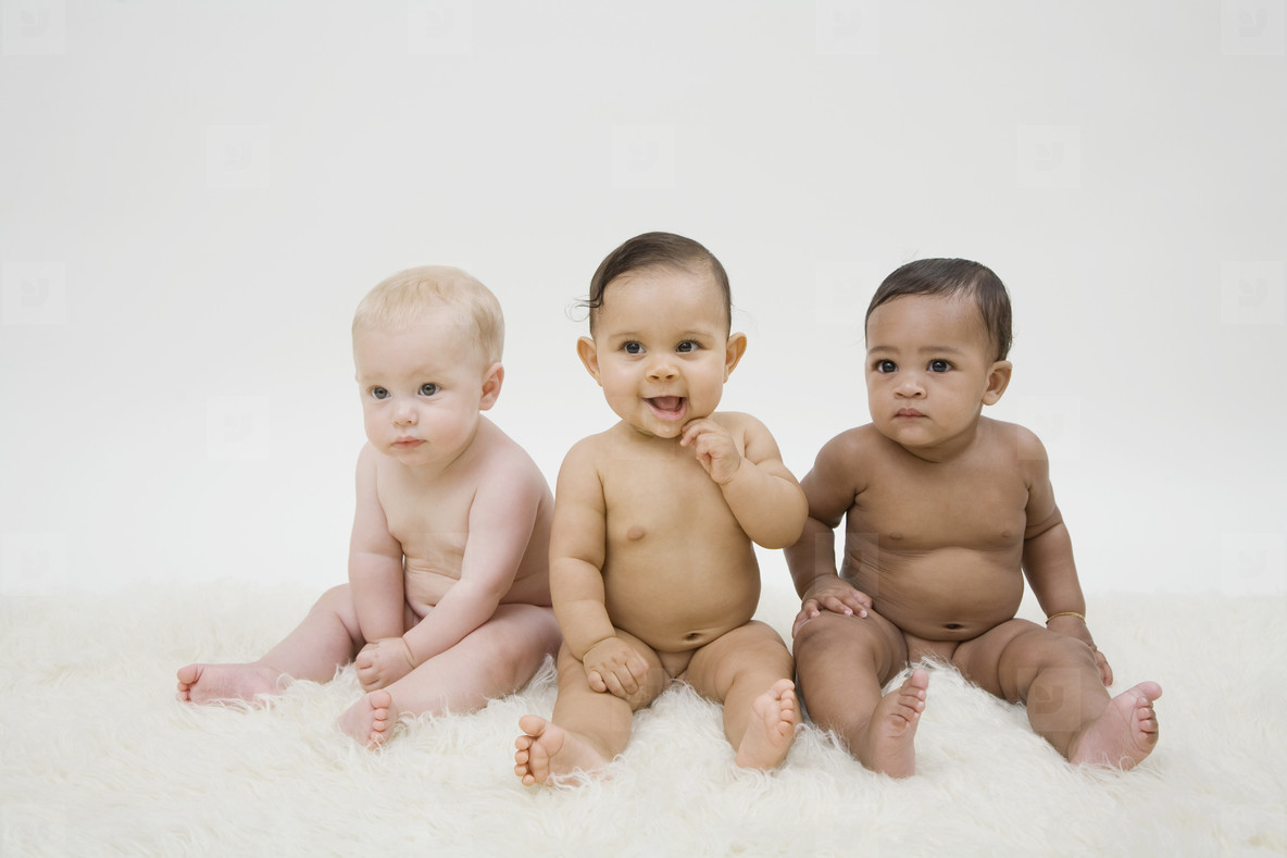 Three naked babies sitting in a row. 