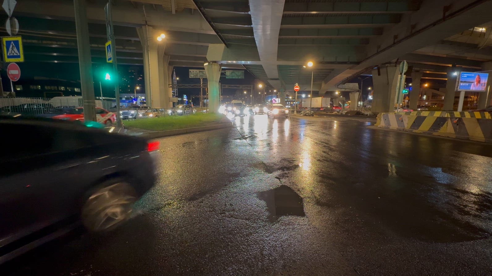 Nighttime urban intersection under highway with wet roads and tr