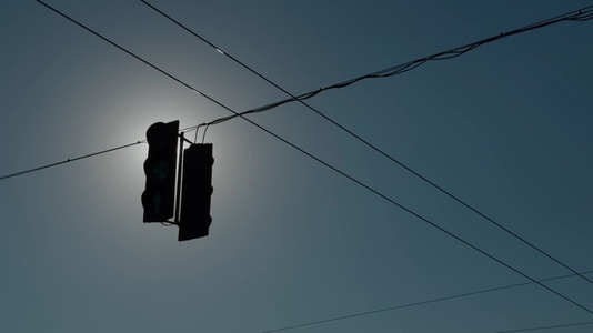 Silhouette of a traffic light against a bright sun and clear sky
