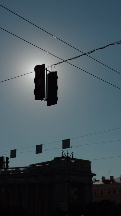 Silhouette of a traffic light against a bright sunlit sky.